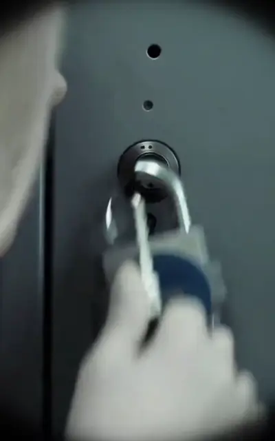 A hand turns a padlock on a locker