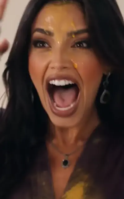 A woman in purple stares shocked as cake is smashed at a bright table