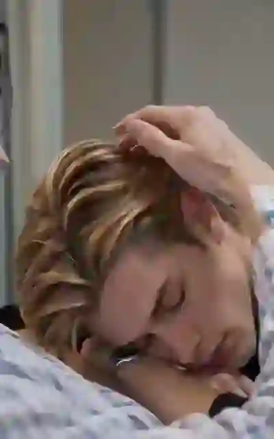 The blonde man's head resting on a lap in the hospital room